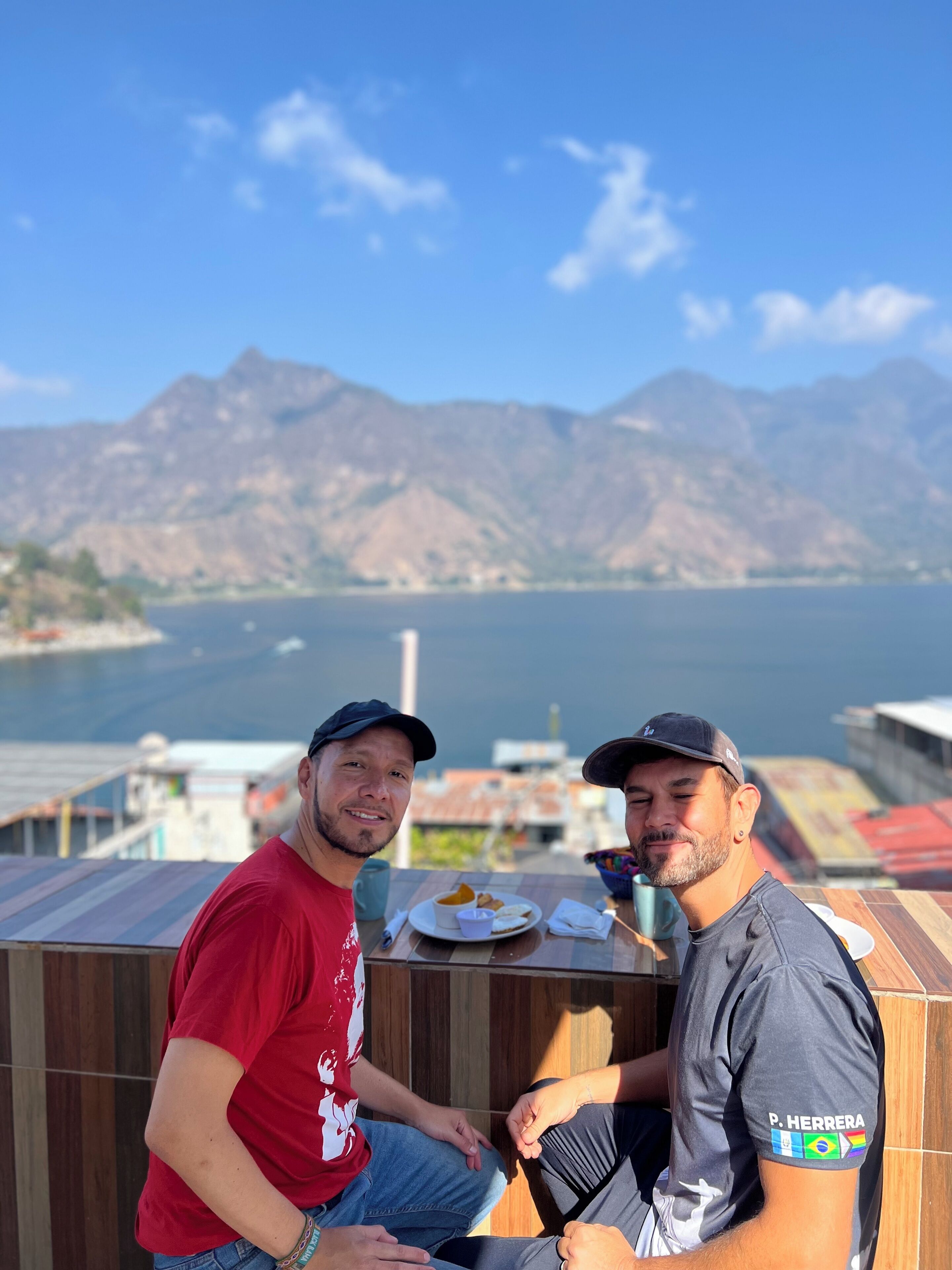 Dos personas sentadas a una mesa con vistas a un lago y montañas al fondo.