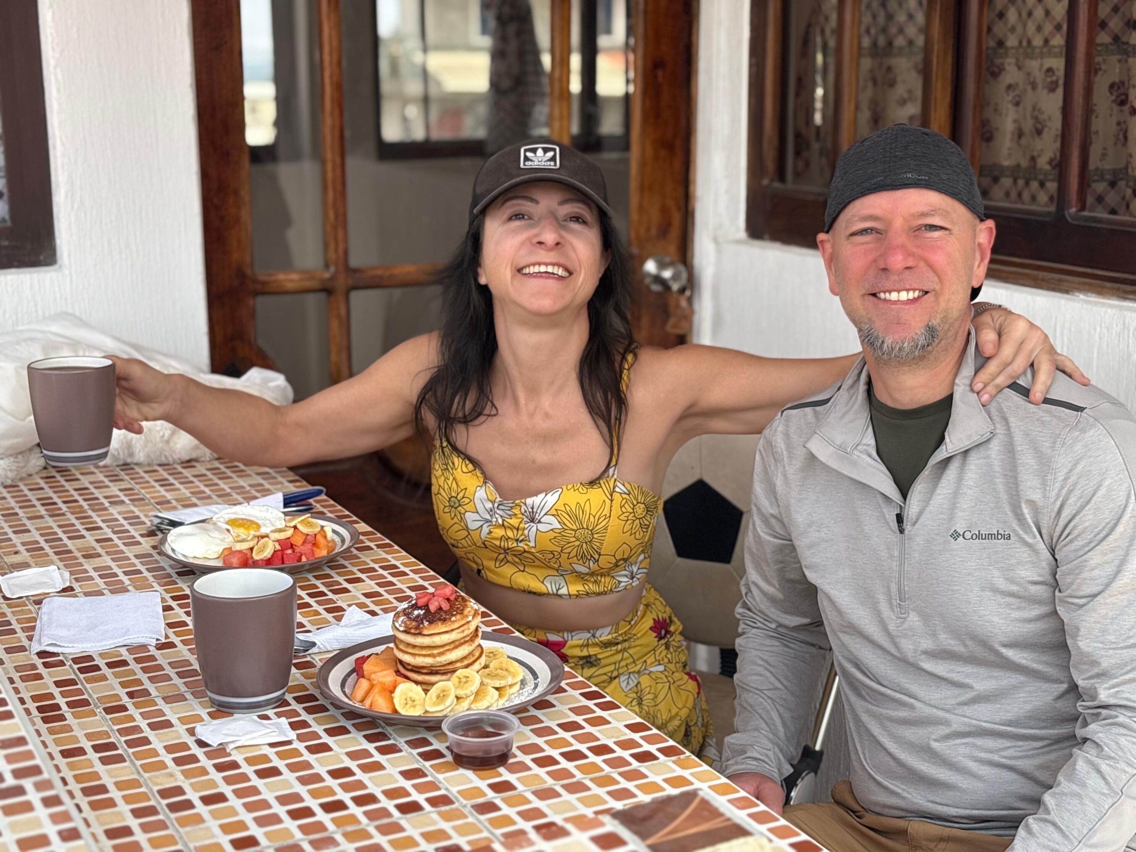 A dining table with a checkered tablecloth, a plate of pancakes with fruit, and a cup of coffee.