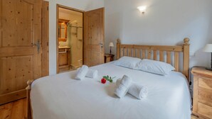 A neatly made bed with white linens and towels, a wooden headboard, and a nightstand with a lamp. - 3BR Balcony & Parking near Argentière, Le Tour (Argentière), France (Le Tour (Argentière))