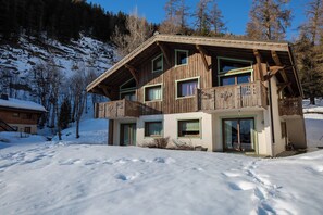 A wooden chalet with a balcony, large windows, and a snow-covered landscape.