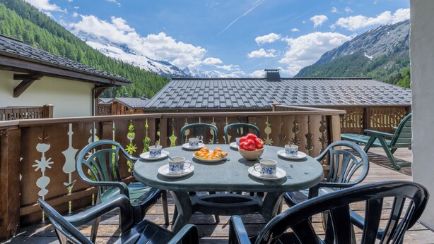 A round table with chairs, a bowl of fruit, and plates with cups, set against a mountainous backdrop. - 3BR Balcony & Parking near Argentière, Le Tour (Argentière), France (Le Tour (Argentière))