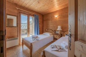 Una habitación de cabaña de madera con dos camas, una ventana con cortinas, una mesita de noche con una lámpara y un espejo.