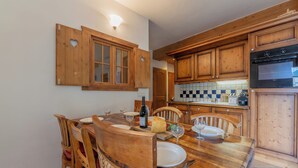 A wooden dining table with chairs, a wine bottle, and a checkered backsplash in the kitchen. - 3BR Balcony & Parking near Argentière, Le Tour (Argentière), France (Le Tour (Argentière))