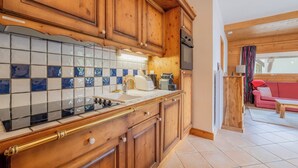 A kitchen with wooden cabinets, a tiled backsplash, and a red couch in the adjacent living area. - 3BR Balcony & Parking near Argentière, Le Tour (Argentière), France (Le Tour (Argentière))