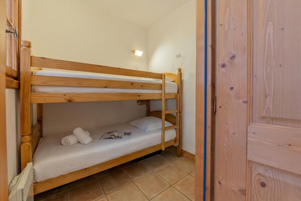 Un lit superposé avec une structure en bois, un matelas blanc et une serviette enroulée sur le lit du bas.