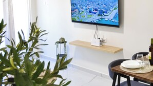 Un salon moderne avec un téléviseur à écran plat fixé au mur, une table à manger avec des chaises et une plante en pot.