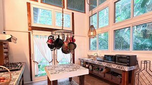 A spacious kitchen with large windows, a hanging pot rack, a tiled table, and a built-in oven. - Casa Azul · Family Retreat & Caribbean Charm (Manzanillo)
