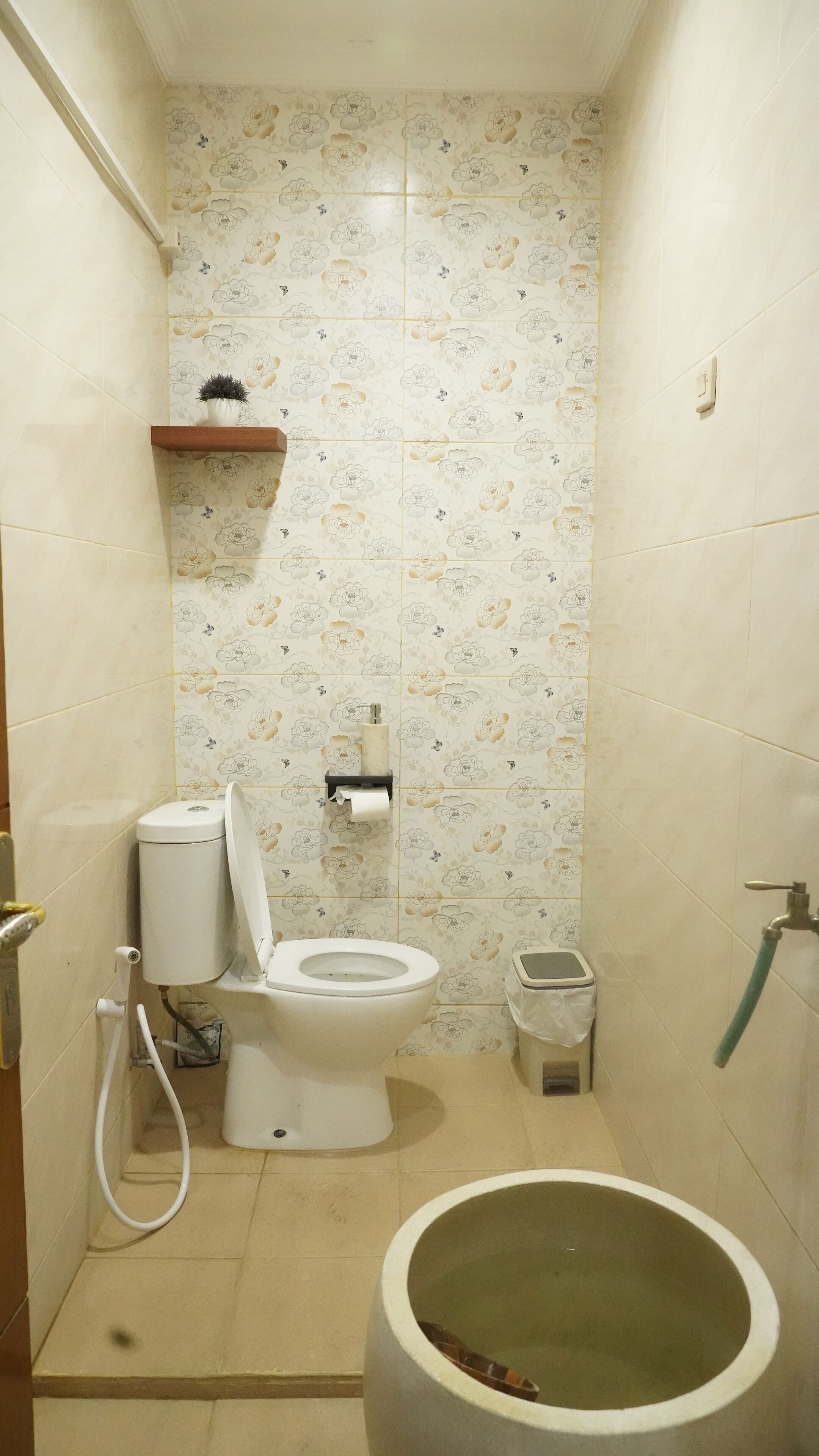 A small, compact bathroom with a toilet, a toilet paper holder, a trash bin, and a shower area.