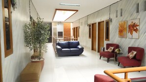 A hallway with a blue sofa, red chairs, a potted plant, and a staircase.