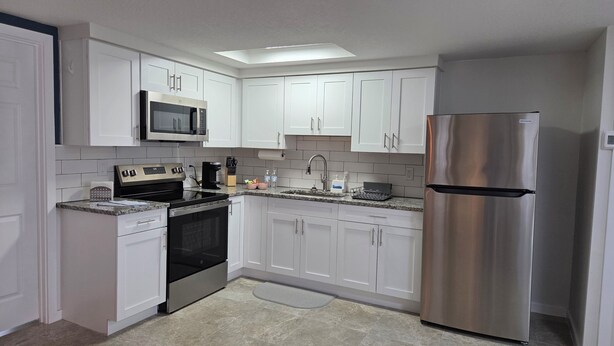 A modern kitchen with white cabinets, stainless steel appliances, and a tiled backsplash. - Peaceful accomodation. Walking distant to Port Richey waterfront restaurants. (Port Richey)