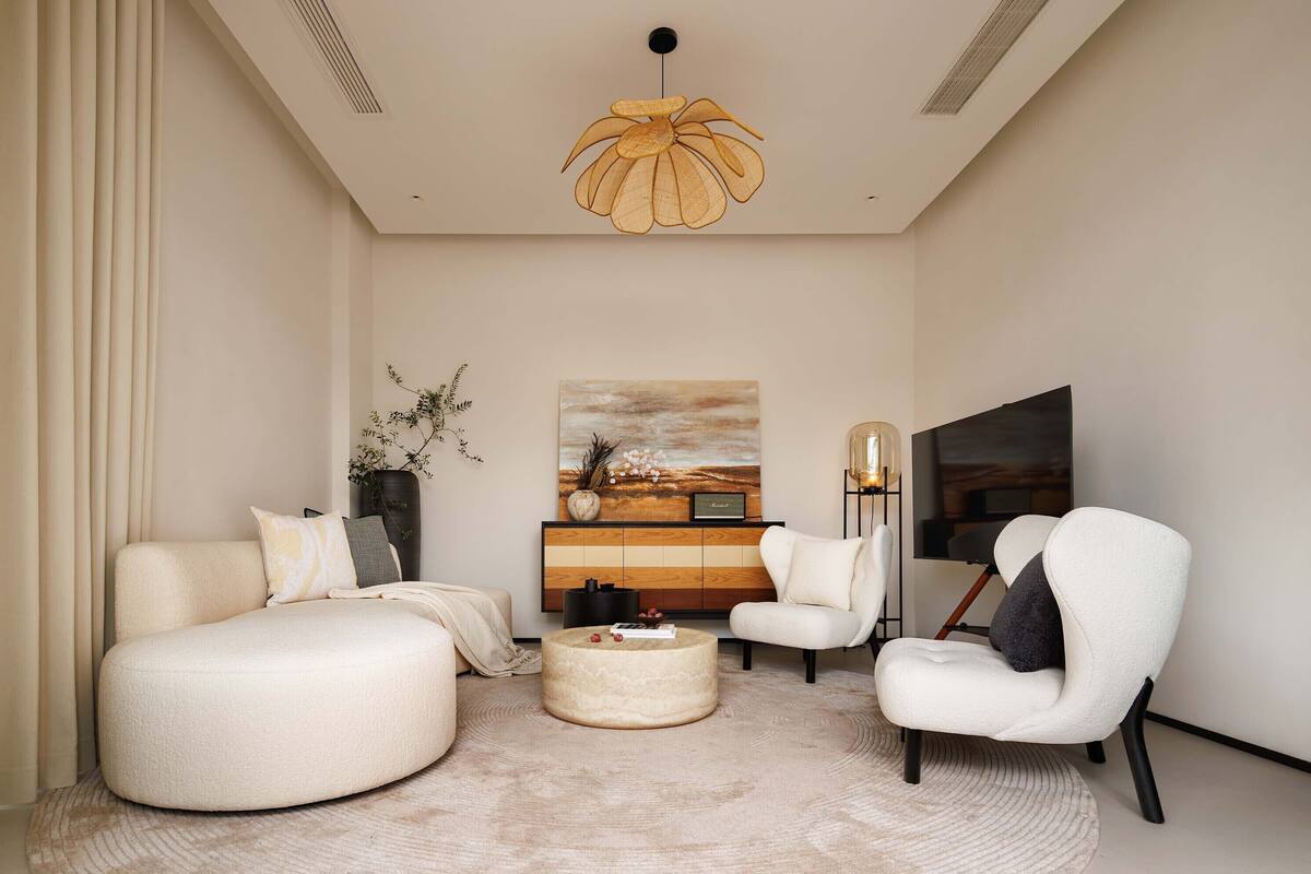 A modern living room with a sofa, armchair, round coffee table, and a large painting on the wall.