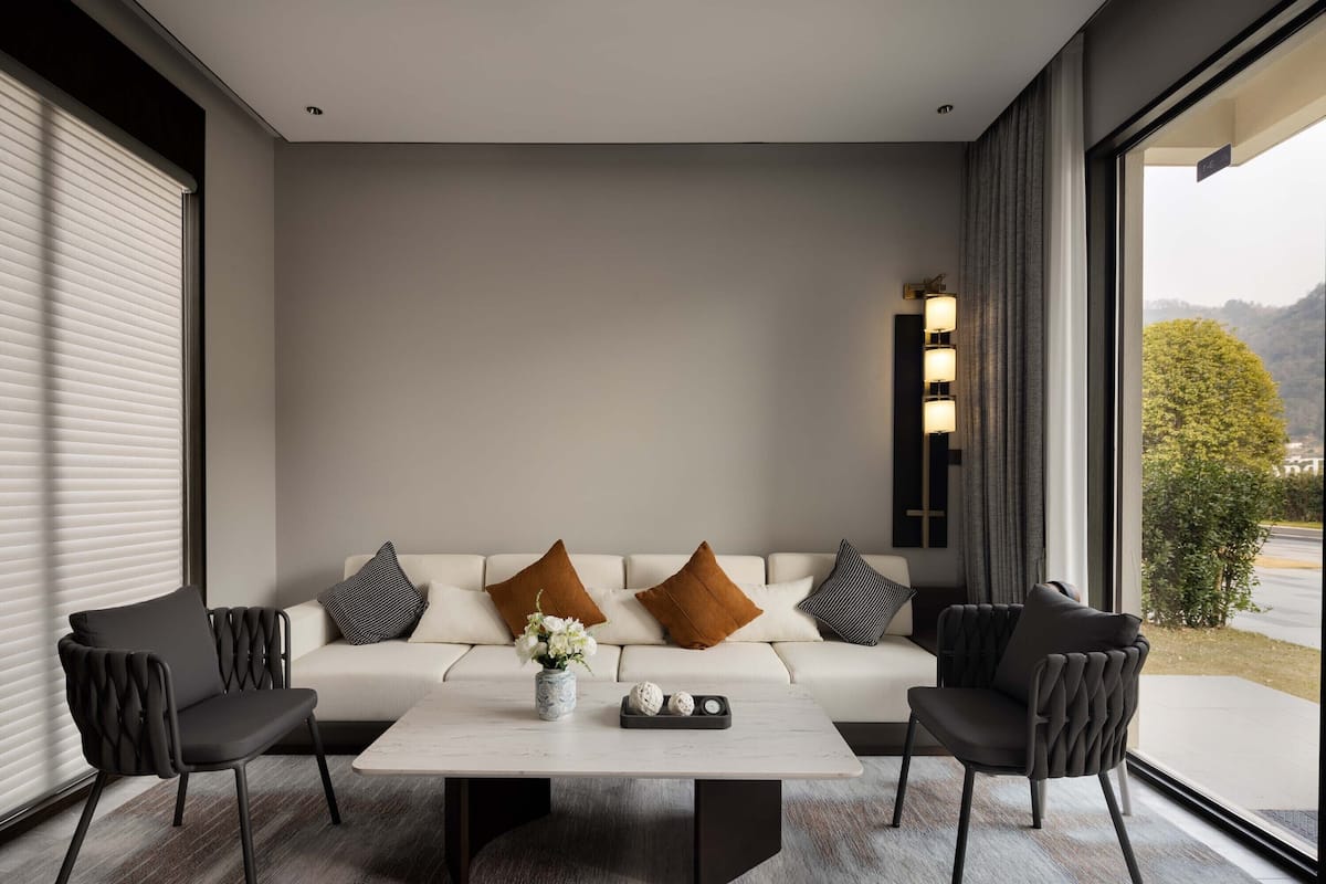 A modern living room with a white sofa, two black chairs, a marble coffee table, and a vase of flowers.
