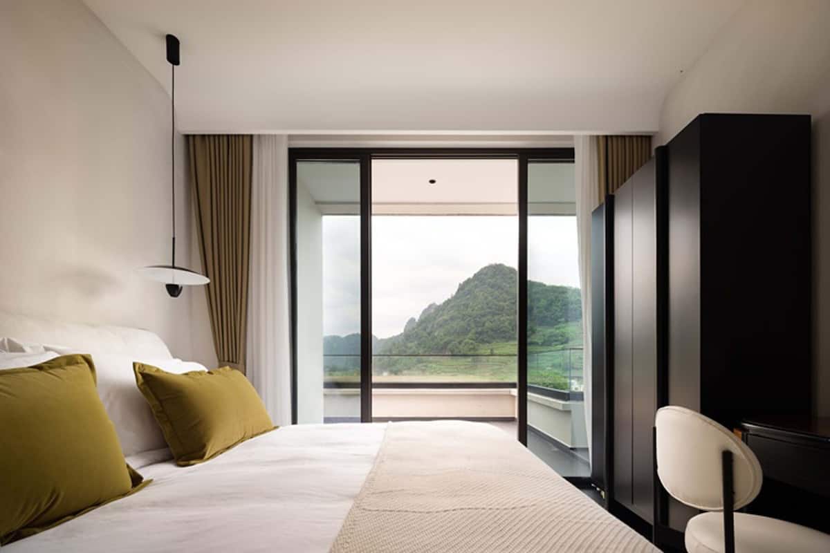 A modern hotel room with a large bed, a desk, and a view of a mountainous landscape.