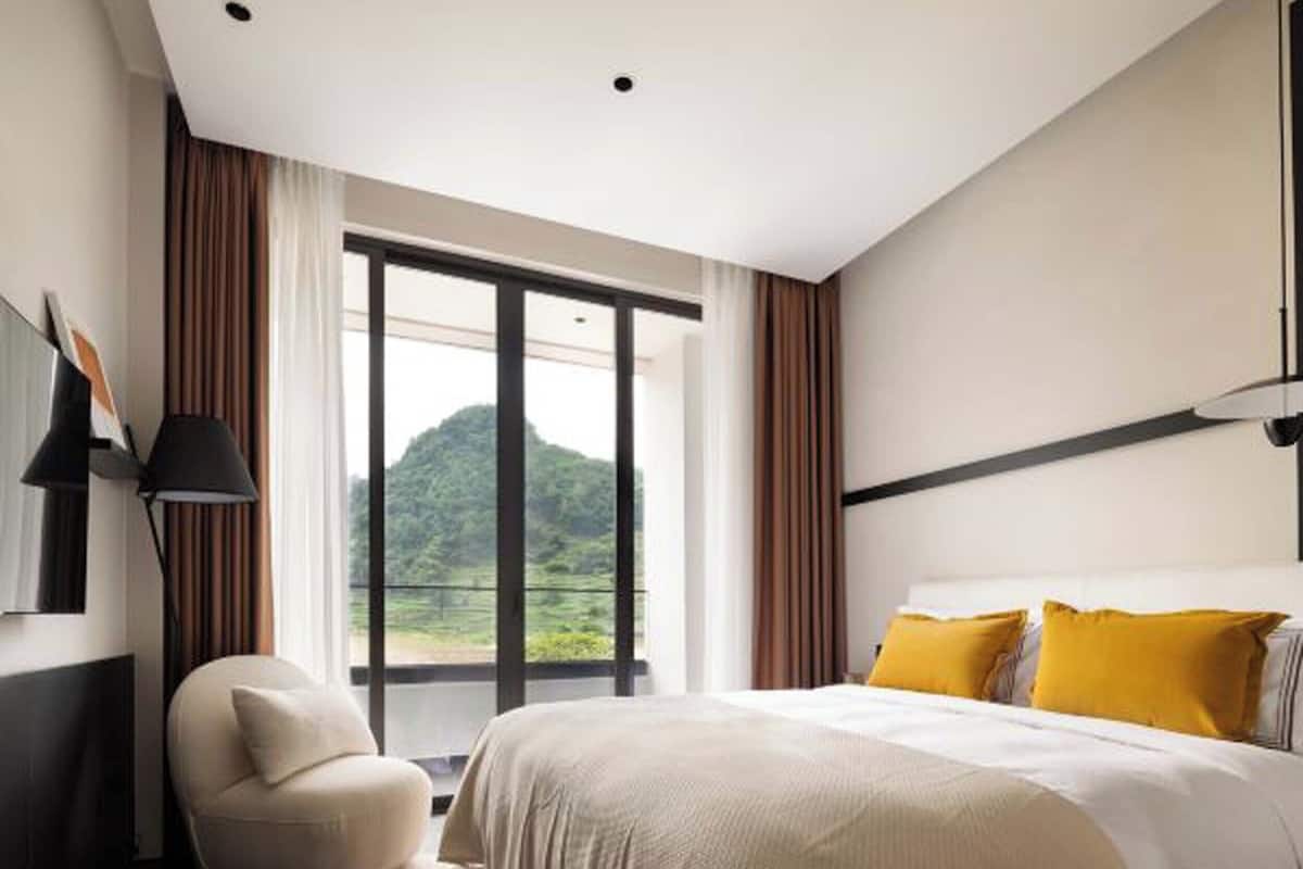 A modern hotel room with a large bed, a chair, and a view of a mountain through a sliding door.