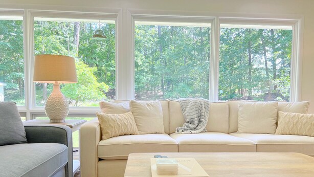 A living room with a beige sofa, a grey armchair, a wooden coffee table, and a lamp.