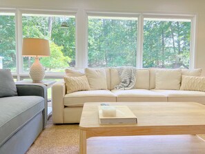 A living room with a beige sofa, a grey armchair, a wooden coffee table, and a lamp.