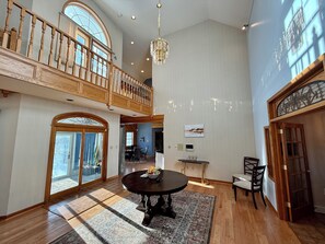 A spacious living area with a high ceiling, wooden staircase, and a chandelier. - Private Mansion Getaway NY (Amsterdam)