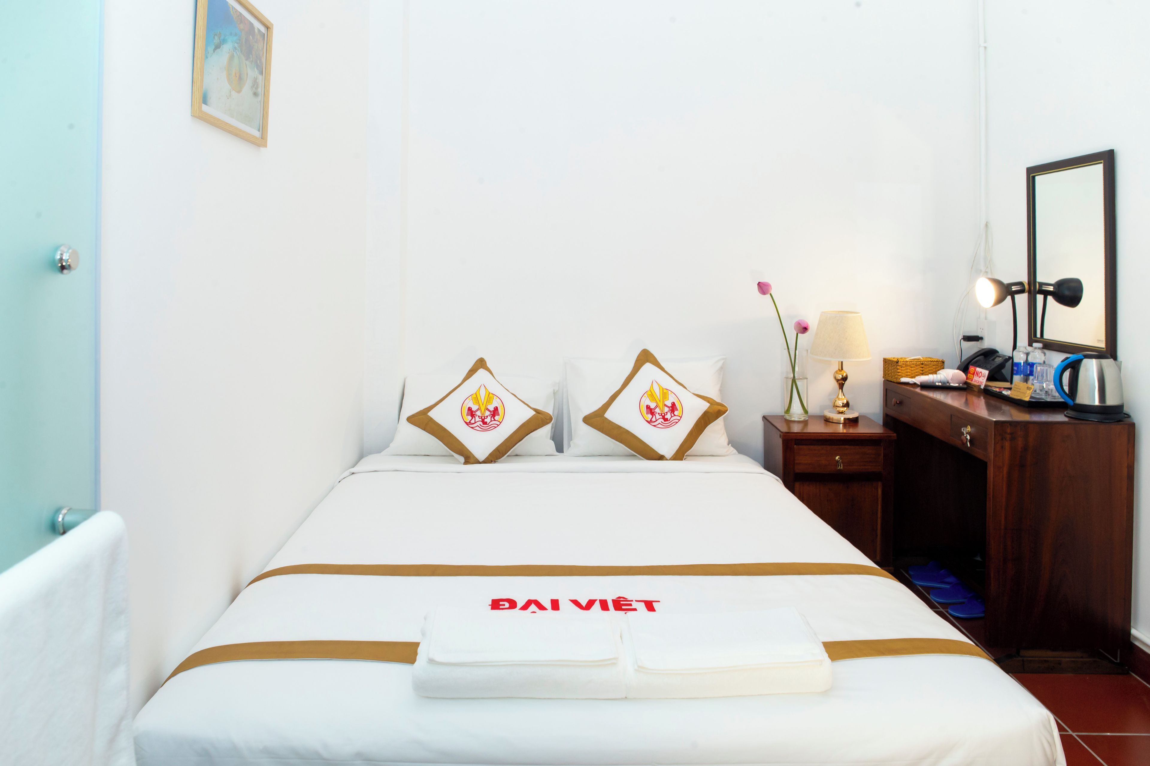 A hotel room with a bed, a nightstand, a mirror, and a wall-mounted picture.