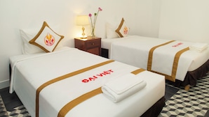Ein Hotelzimmer mit zwei Betten, beide mit weißer Bettdecke und brauner Streifen. Es gibt einen Nachttisch mit Lampe und eine Vase mit Blumen.