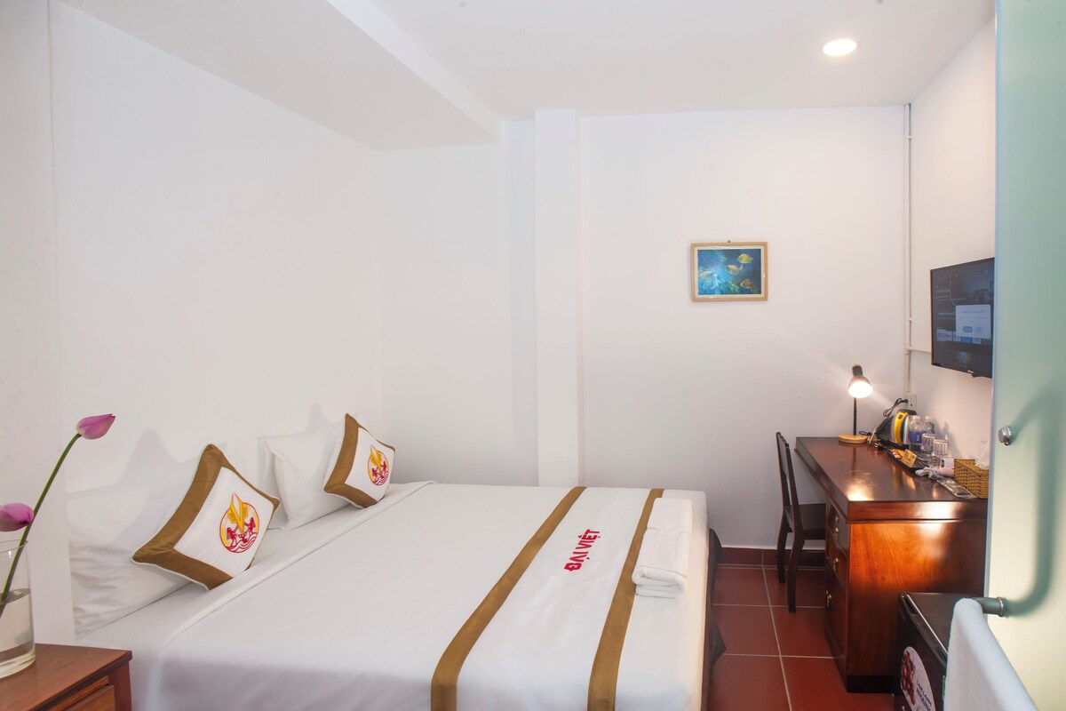 A hotel room with a bed, a desk, a chair, a lamp, and a picture on the wall.