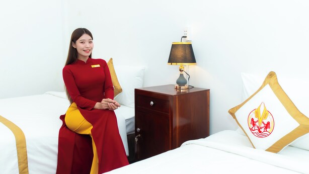 A hotel room with a bed, a nightstand with a lamp, and a pillow with a logo. - The Rice Hotel & Tour - 195 De Tham (Ho Chi Minh City)