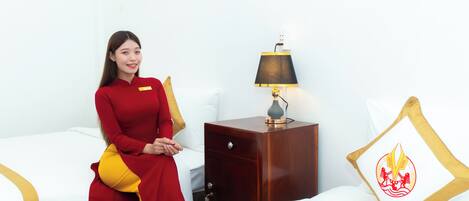 A hotel room with a bed, a nightstand with a lamp, and a pillow with a logo.