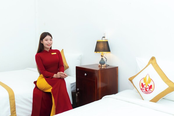 A hotel room with a bed, a nightstand with a lamp, and a pillow with a logo. - The Rice Hotel & Tour - 195 De Tham (Ho Chi Minh City)