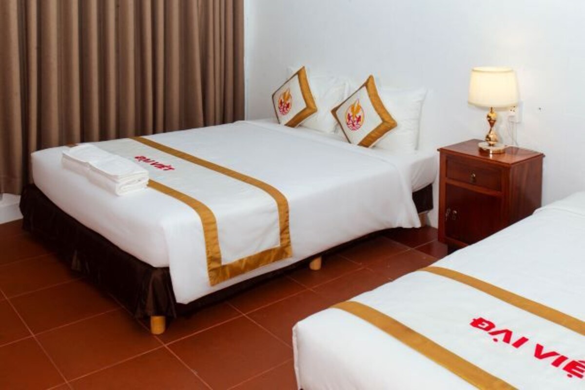 A hotel room with two beds, a nightstand, a lamp, and a curtain.