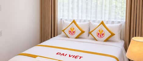 Une chambre d’hôtel avec un lit, des rideaux, une fenêtre et une table de chevet avec une lampe.