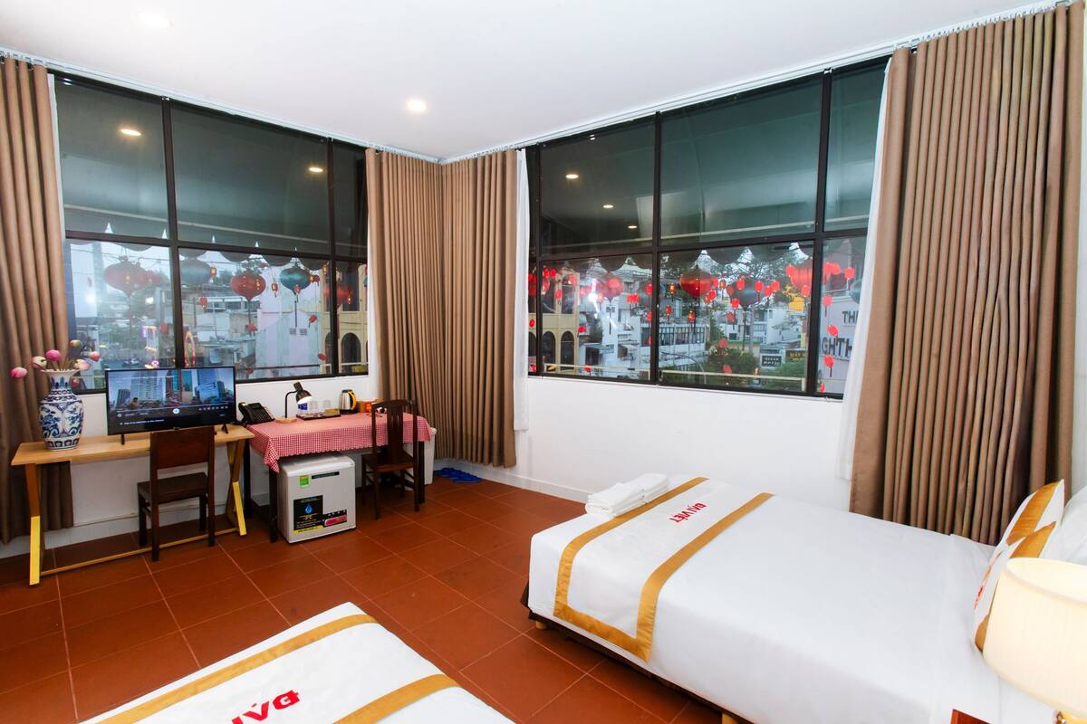 A hotel room with a desk, computer, chair, and a bed with a view of the city.