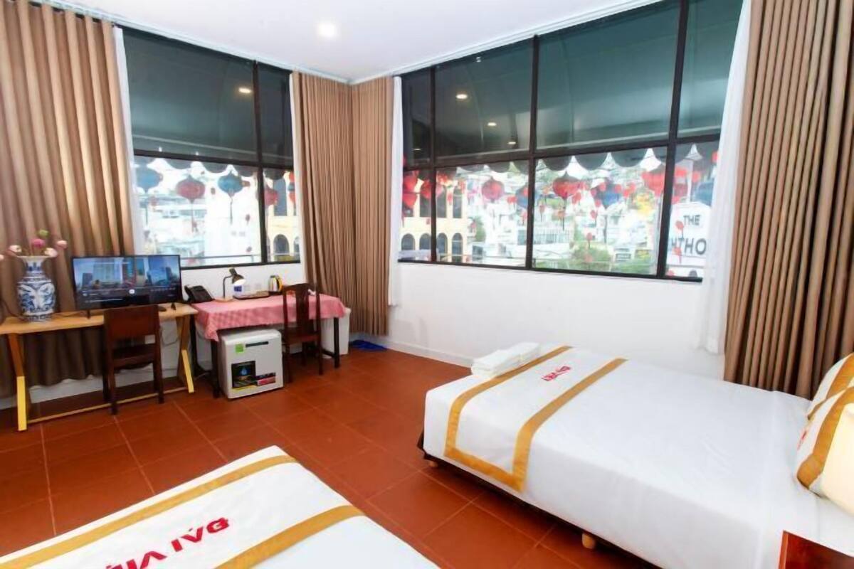 A hotel room with a bed, a desk, a chair, a small table, and a window with curtains.