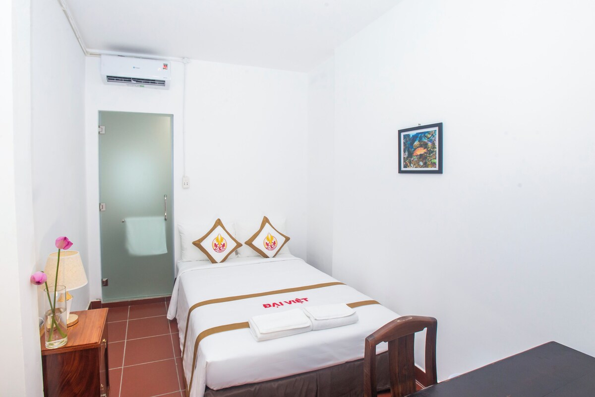 A hotel room with a bed, a small table with a lamp, and a picture on the wall.