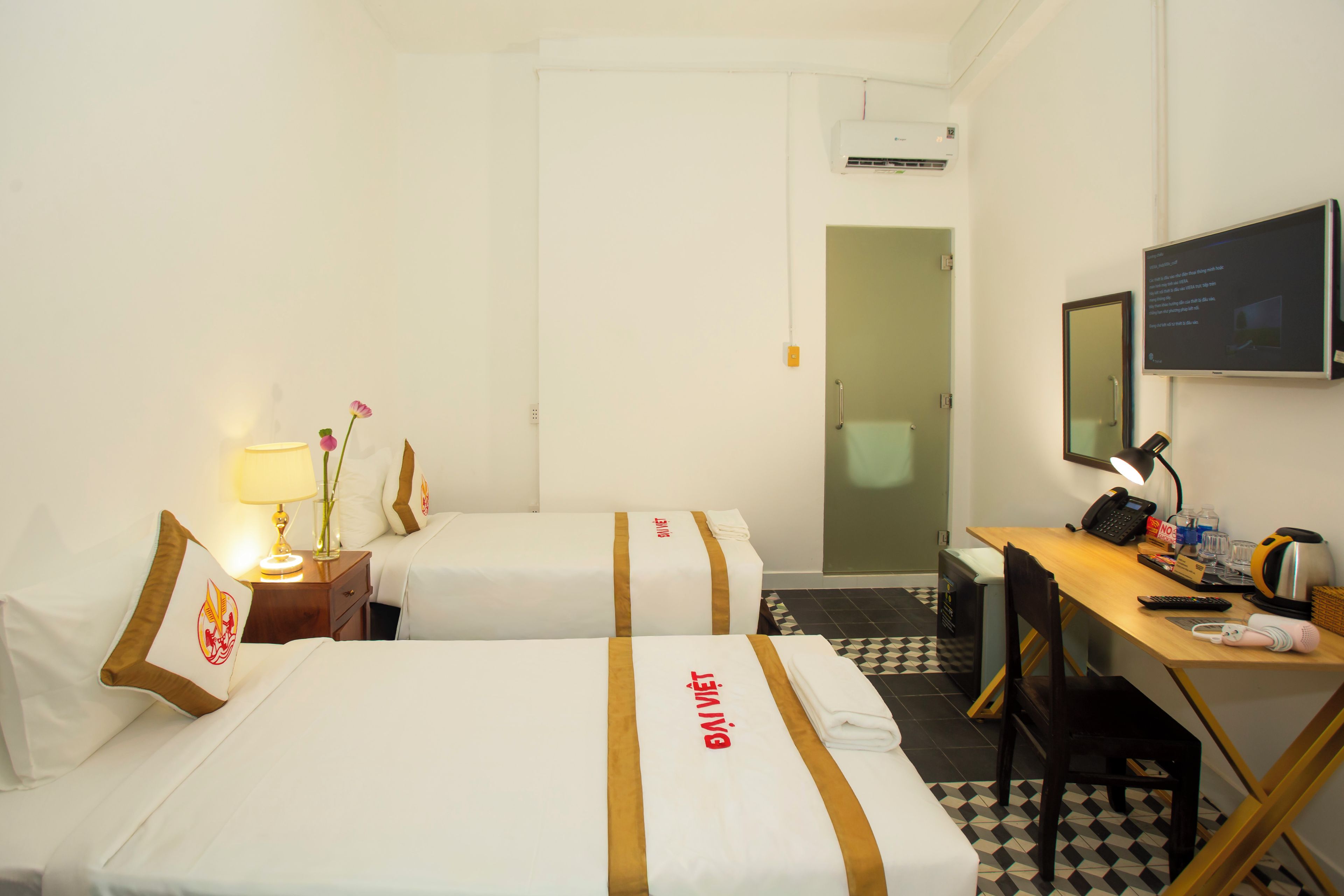 A hotel room with two beds, a desk, a chair, a TV, and a bathroom door.