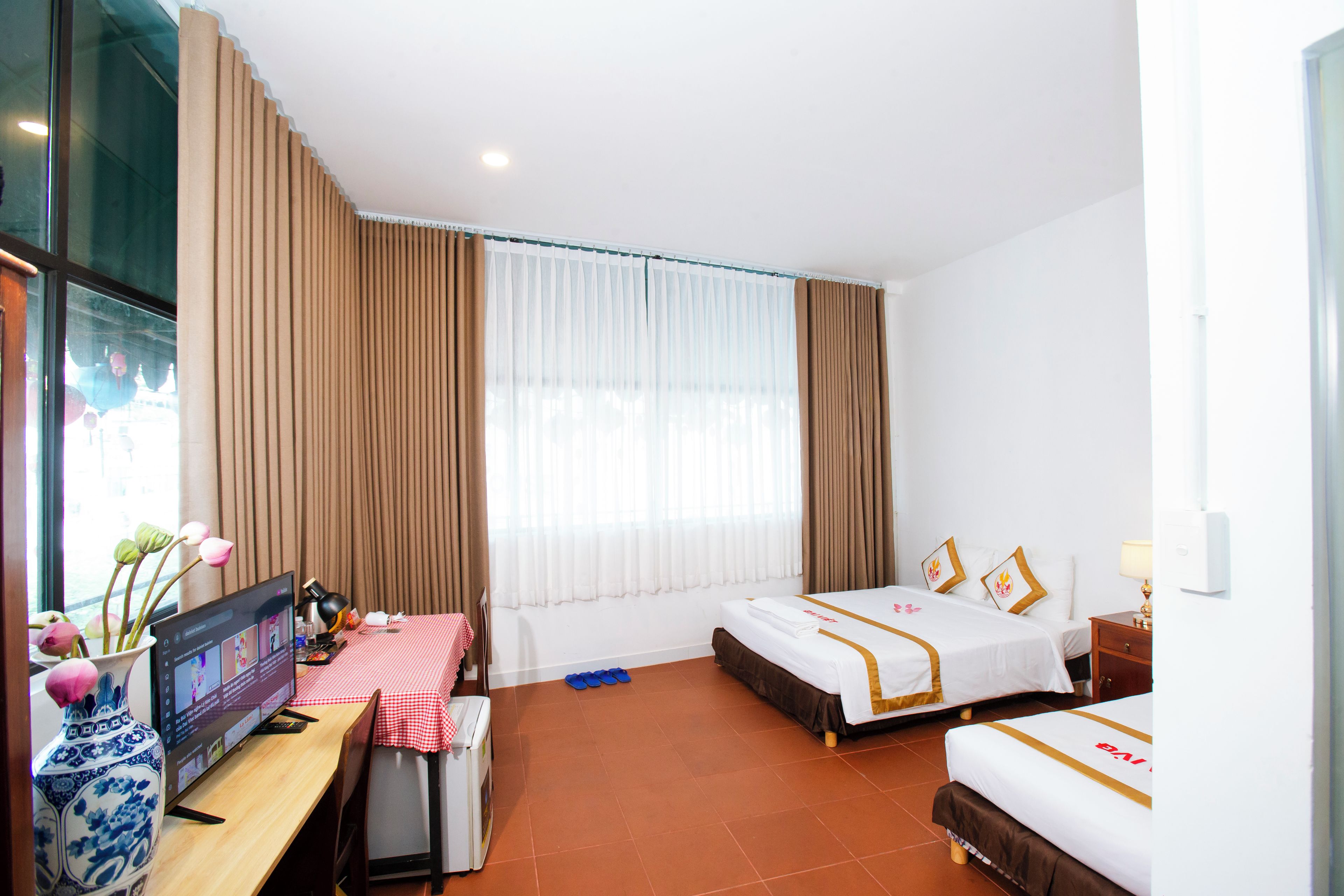A hotel room with a bed, a desk, a chair, a TV, and a window with curtains.