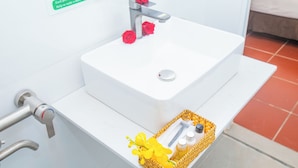 Ein Waschbecken mit Wasserhahn, ein Handtrockner und ein gelber Korb mit Pflegeprodukten.