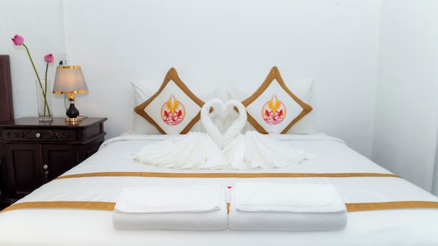 Ein ordentlich bezogenes Bett mit einer herzförmigen Handtuchgestaltung und passenden Kissen.