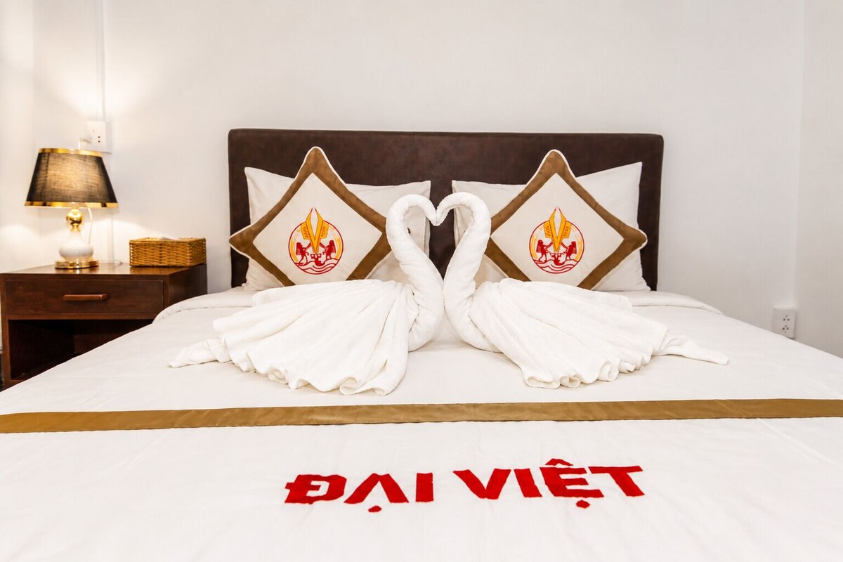 A bed with towels arranged in swan shapes and a bedspread with 'DAI VIET' text.