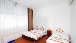 A hotel room with two beds, a window with curtains, a nightstand with a lamp, and a pair of slippers on the floor. - The Rice Hotel & Tour - 195 De Tham (Ho Chi Minh City)