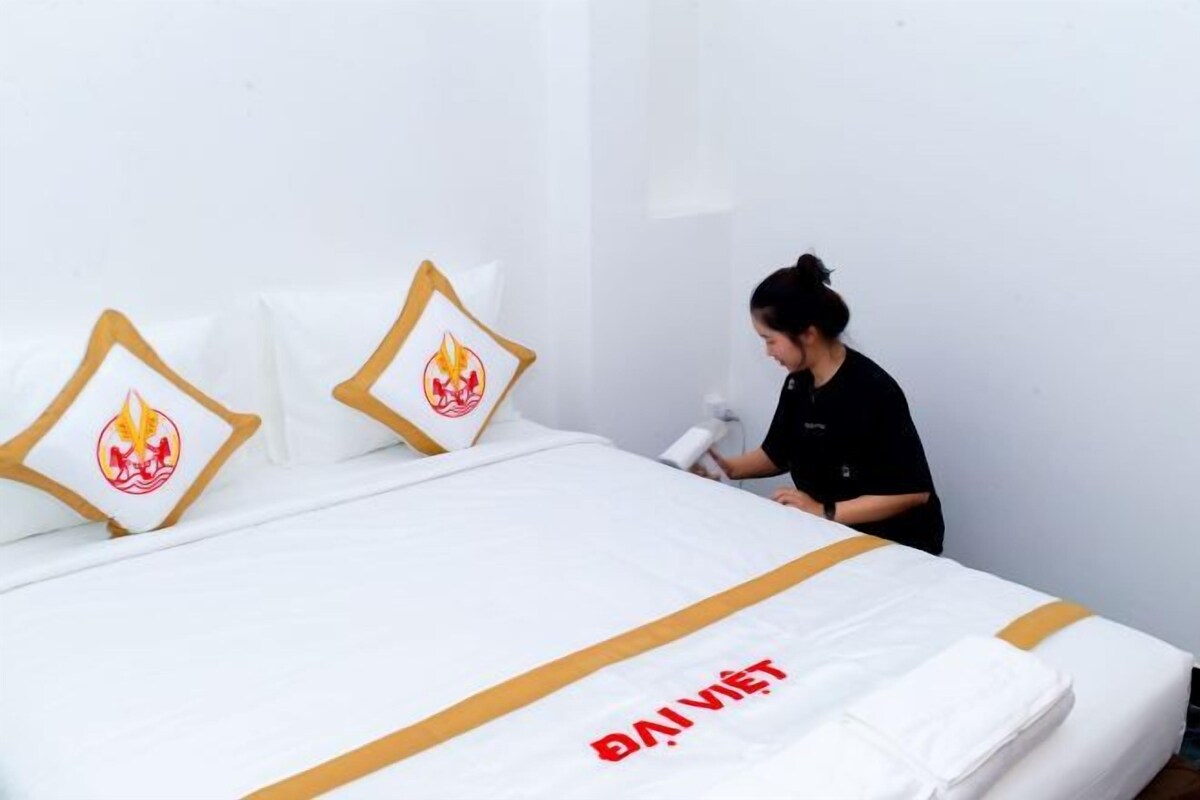 A bed with a white cover and a logo, a pillow with a flame design, and a person standing by the bed.