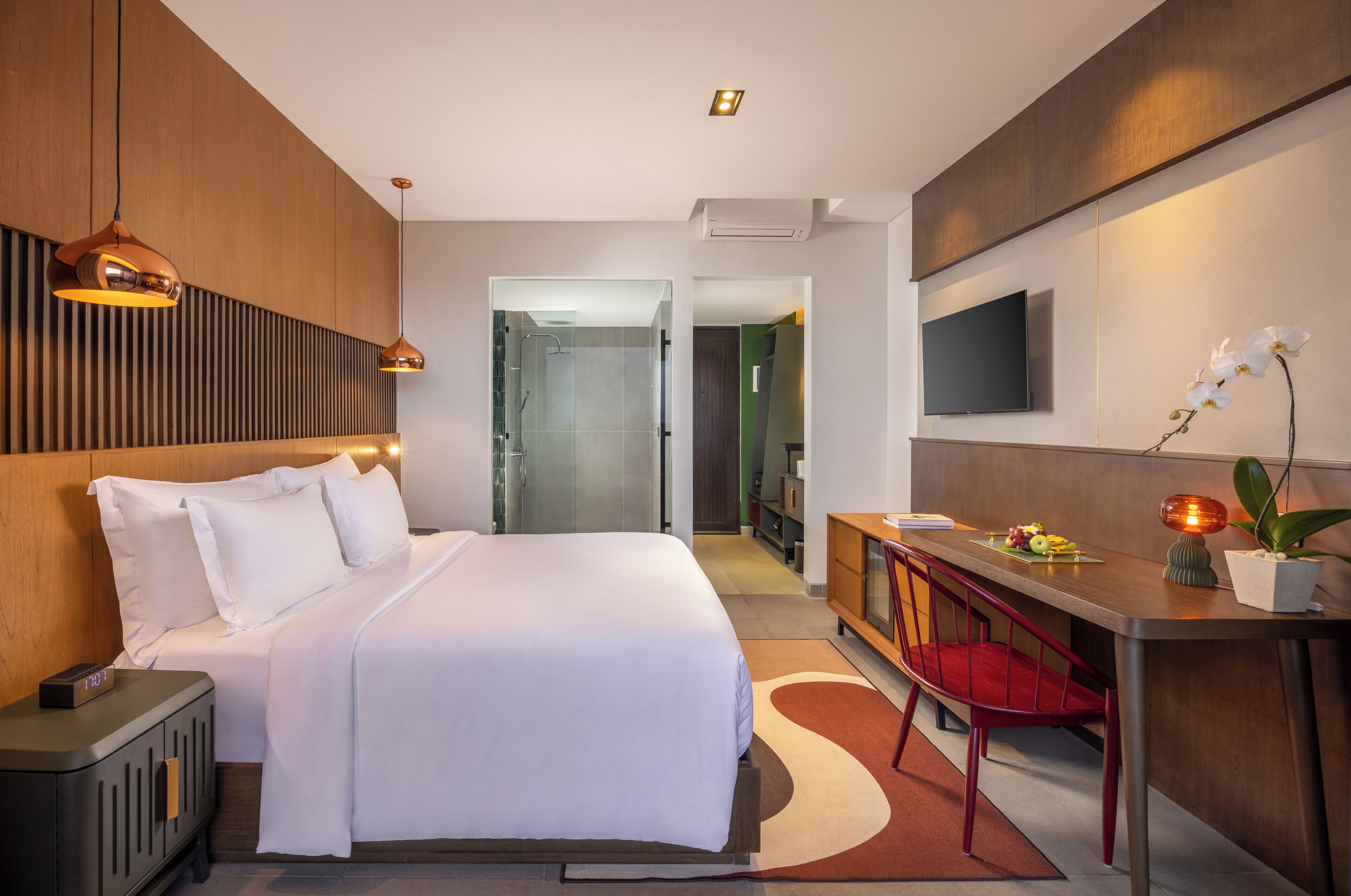 A modern hotel room with a large bed, a desk with a chair, a TV mounted on the wall, and a shower area.
