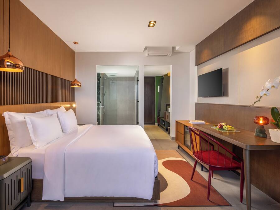 Una habitación de hotel moderna con una cama grande, un escritorio con una silla, un televisor montado en la pared y una zona de ducha.