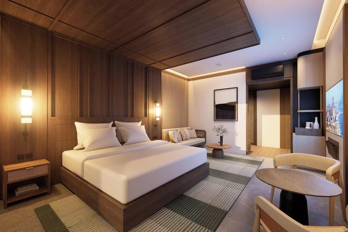 A modern hotel room with a large bed, bedside tables, a seating area, and a TV.