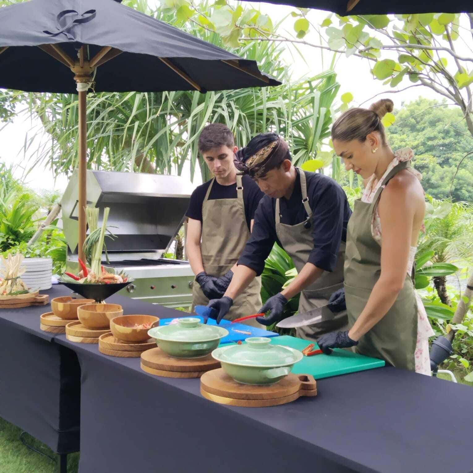 A group of people preparing food outdoors with a grill and various bowls on a table.