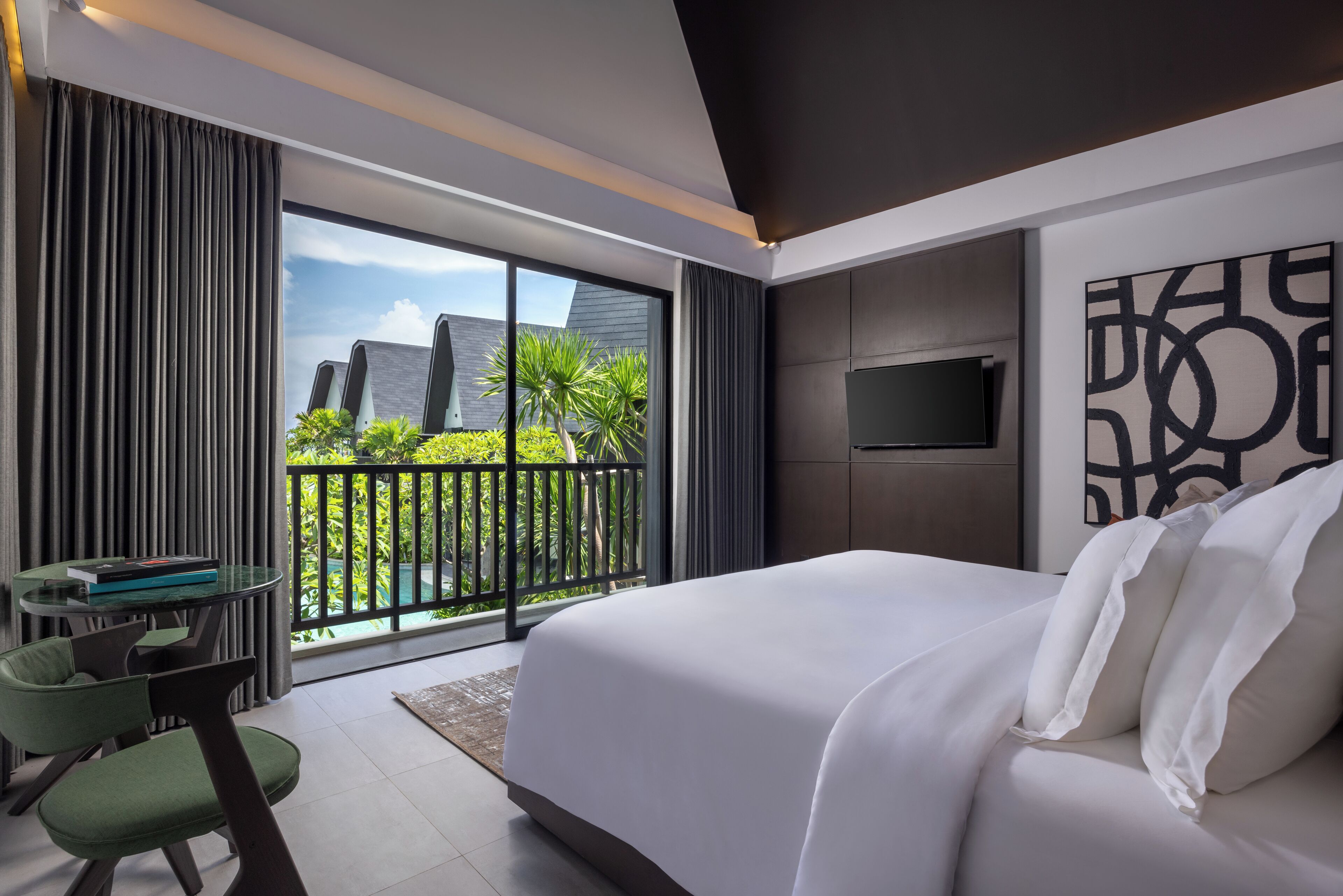 Camera d'albergo moderna con un letto grande, una TV e un balcone con vista sul verde.
