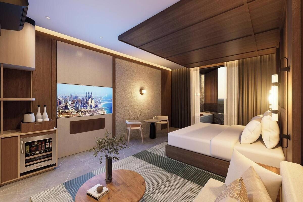 A modern hotel room with a large TV, a sofa, a small table, and a decorative plant.