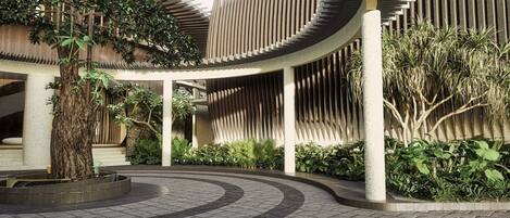 A modern building with a curved facade, a circular water feature, and lush greenery.