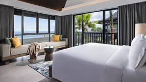 Een moderne hotelkamer met een groot bed, een bank met kussens, uitzicht op zee en een balkon met palmbomen.