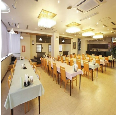 A spacious dining hall with multiple tables and chairs, ceiling lights, and a stage area.