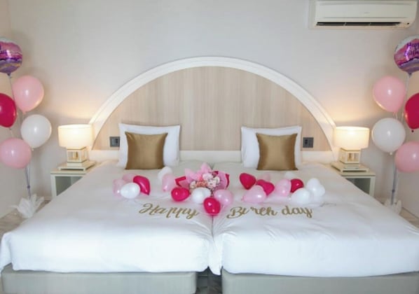 Una cama doble con adornos de 'Feliz Cumpleaños', dos mesitas de noche con lámparas y un cabecero de madera.