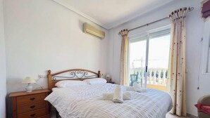 Ein ordentlich bezogenes Bett mit weißen Leinen, ein Nachttisch aus Holz mit Schubladen und ein Fenster mit Vorhängen.